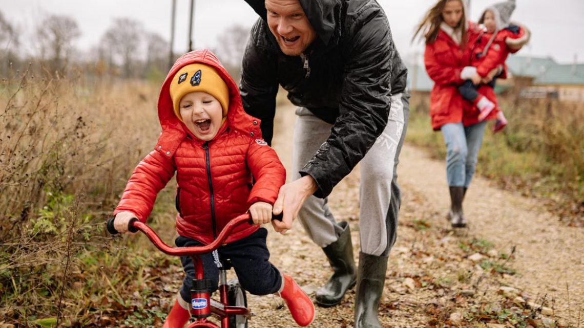 Father helping son ride a bicycle on a fall day while mother and daughter watch.
