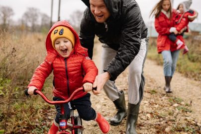 Father helping son ride a bicycle on a fall day while mother and daughter watch.