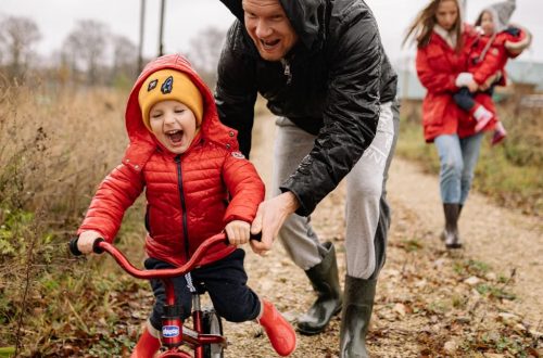 Father helping son ride a bicycle on a fall day while mother and daughter watch.