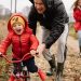 Father helping son ride a bicycle on a fall day while mother and daughter watch.